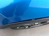 the rear end of a blue car with a person standing next to it