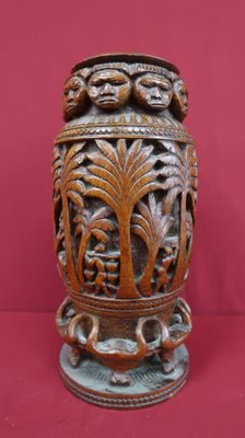 un vase en bois orné de sculptures sur un fond rouge