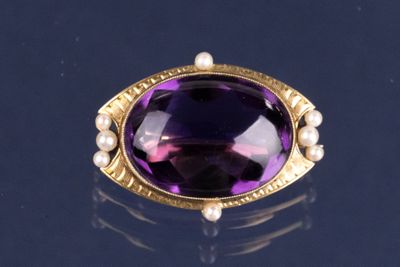 une photo d'une bague ornée d'une pierre violette et d'une perle, posée sur un fond noir