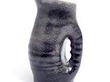 a black vase with a hole in it on a white surface