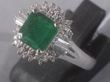 an emerald and diamond ring on display on a black stand