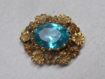 an image of a brooch with a blue stone surrounded by flowers
