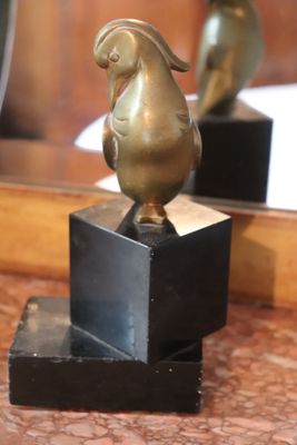 a gold bird statue on a black stand in front of a mirror