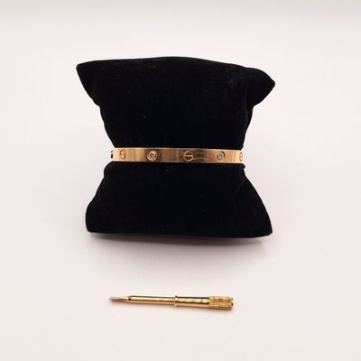 une photo représentant un bracelet en or et un stylo posés sur un sac en velours noir
