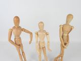 three wooden mannequins standing next to each other on a white surface