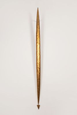 a gold colored dagger with a pointed tip on a white surface