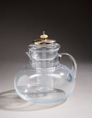 a glass teapot with a gold lid on a table