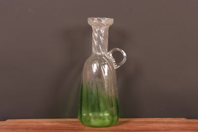 un vase en verre vert muni d'une anse, posé sur une table en bois