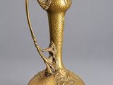 a gold vase with a bird on the handle on a gray background