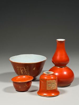 Trois vases rouges, un bol et une tasse sont posés sur une table.