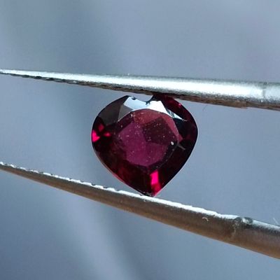 une image représentant un diamant en forme de cœur, de couleur rubis, tenu par une pince à épiler