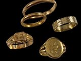 trois bagues en or et une bague ornée d'une pièce de monnaie sur fond noir