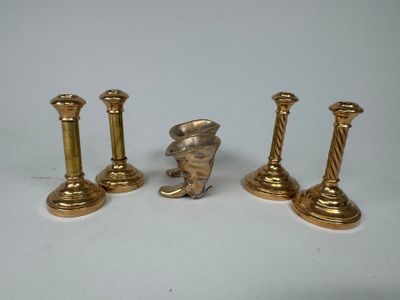 trois bougeoirs en or et une figurine posés sur un support blanc