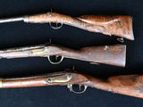 three old guns are lined up on a black surface