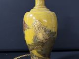 a yellow vase with a bird on it on a table