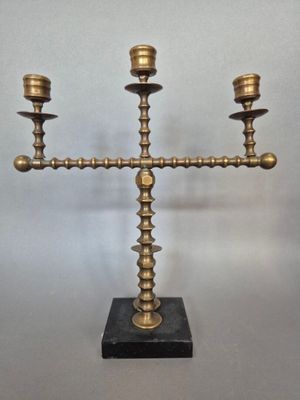 un candélabre ancien en laiton à trois bougies, posé sur un socle en marbre
