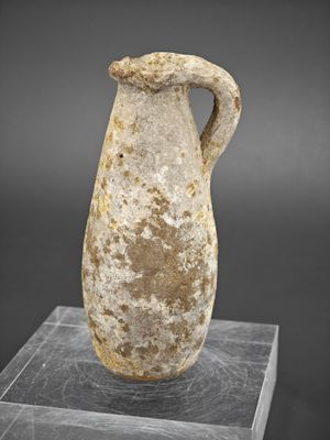 un vase en pierre muni d'une anse, posé sur un socle transparent