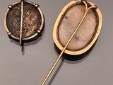 two antique brooches on a gray surface one has a coin and the other has a pin