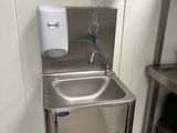 un lavabo en acier inoxydable dans une salle de bains, avec un distributeur de serviettes fixé au mur