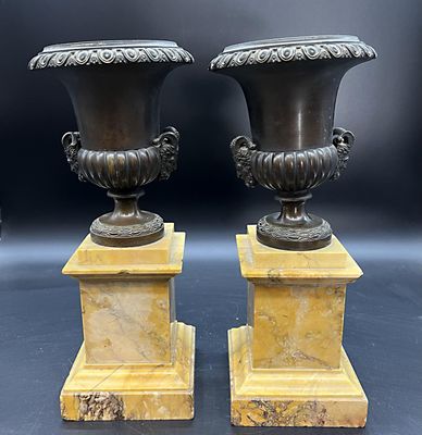 paire d'urnes anciennes en bronze reposant sur des socles en marbre, sur fond noir