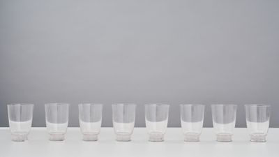 six clear glasses lined up in a row on a white table