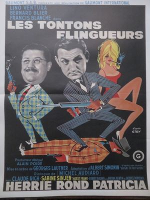 une affiche du film « Les Tontons », sur laquelle figurent deux hommes en costume et une femme en