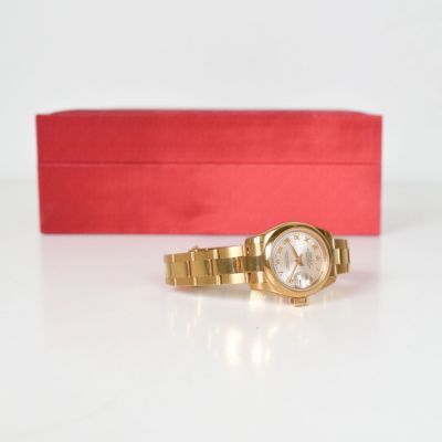 une montre en or posée sur une boîte rouge, avec une boîte rouge en arrière-plan