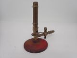 un microscope ancien en laiton posé sur un socle rouge, sur fond blanc