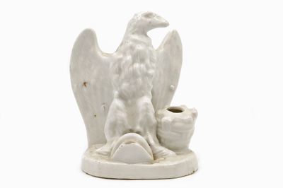 une statue blanche représentant un oiseau tenant une tasse dans son bec