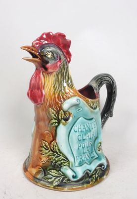 un coq en céramique qui tient une pancarte dans son bec