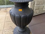 un vase noir posé sur le trottoir, à côté d'un mur de briques