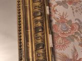 a gold framed mirror on a wall with a floral wallpaper