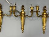 three antique brass wall sconces with candles on each of them