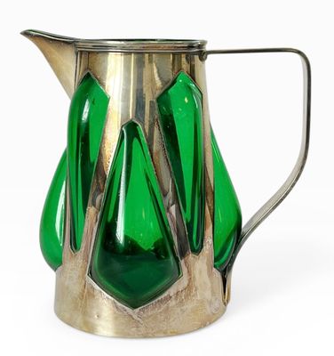 un pichet en verre vert muni d'une anse en métal, posé sur une surface blanche