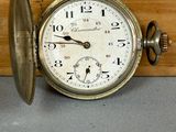 une vieille montre de poche posée sur une table, à côté d'un morceau de bois