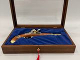 une boîte en bois contenant un pistolet, posée sur un tissu bleu