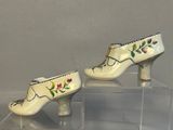 pair of porcelain shoes with painted flowers on them sitting on a clear platform