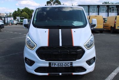 une camionnette blanche ornée d'une bande noire et orange, garée sur un parking