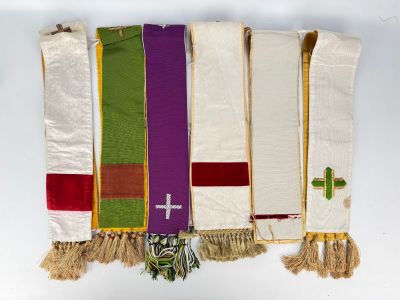 several different colors of cloth hanging on a wall with a cross on it
