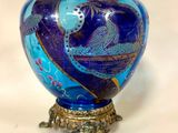 un vase en verre bleu avec un socle doré posé sur une table