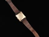 a gold watch with a brown leather strap on a black background