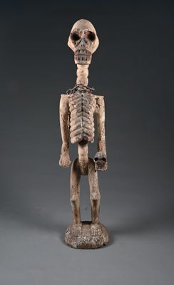 une figurine en bois représentant un squelette debout sur une surface grise