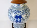un vase bleu et blanc muni d'un couvercle en bois, posé sur un socle