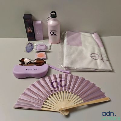a table with a fan, a bottle of lotion, a bag, and other items on it