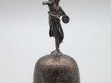 une cloche ancienne en bronze surmontée d'une statue représentant une femme tenant un panier