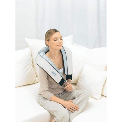 La femme est assise sur le canapé, le cou enveloppé dans une serviette.