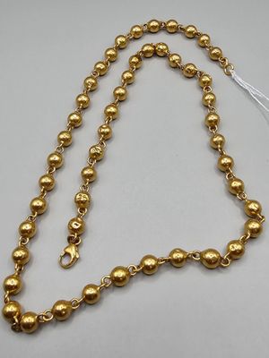 a gold beaded necklace with a tassel on a white background