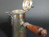 an antique silverplated coffee pot with wooden handle on a black background