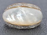 a close up of a ring with a large white pearl and diamonds