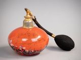 un petit flacon de parfum orange muni d'une poignée noire, posé sur une surface blanche